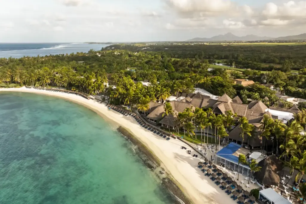 Sicht von oben auf den weißen Traumstrand und das luxuriöse Constance Belle Mare Plage Hotel auf Mauritius, umrahmt von Palmen und tropischer Vegetation. Das Hotel kann bei Fenners Reisen gebucht werden.