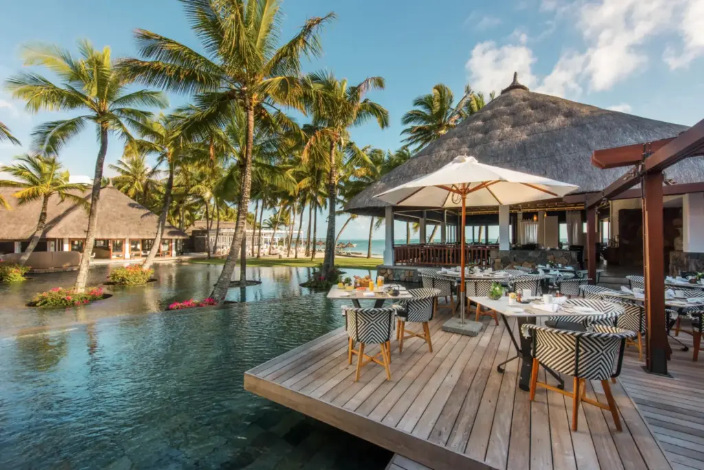 Restaurant des Constance Belle Mare Plage Mauritius - Tische direkt am Pool, mit Blick auf Palmen und das Meer im Hintergrund