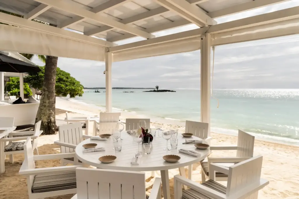 Weißer Tisch und Stühle direkt am Strand - hervorragende Kulinarik mit den Füßen im Sand von Mauritius. Buchen Sie jetzt Ihren Traumurlaub bei Fenners Reisen!