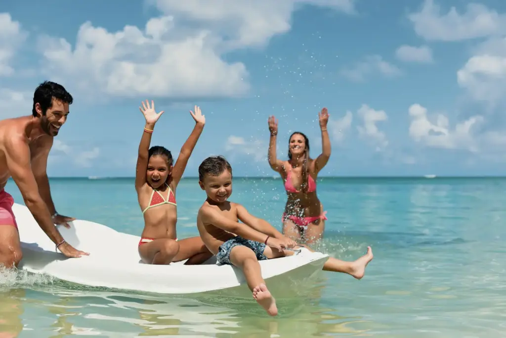 Kinder lassen sich von ihren Eltern auf einem Boot durch den türkisen Ozean ziehen - Spaß ist im Familienurlaub auf Mauritius garantiert, zum Beispiel im Constance Sakoa Boutik Hotel, buchbar bei Fenners Reisen.