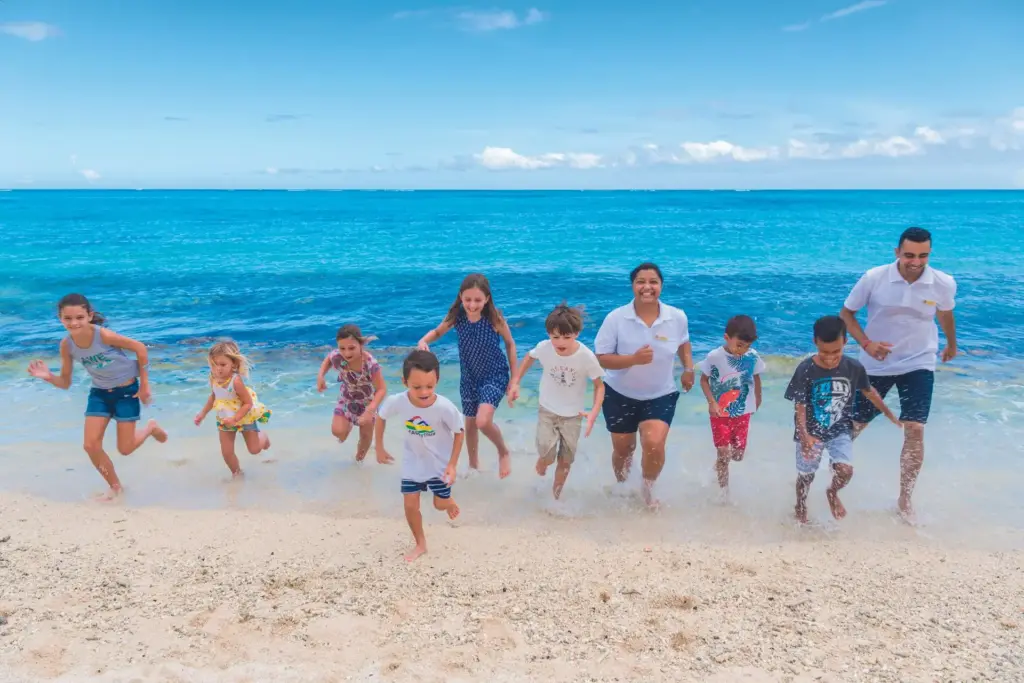 Eine Gruppe von Kindern rennen in Begleitung erfahrener Kinderbetreuer über einen puderweißen Strand. Die Trauminsel Mauritius hat auch für Kinder viel zu bieten! Katharina Fenners organisiert Ihren perfekten Mauritius-Familienurlaub.