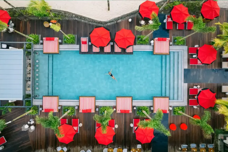 Blick von oben auf eine im Pool schwebende Frau, umrahmt von Sonnenschirmen im knalligen Rot - die LUX Hotels auf Mauritius stehen für Lifestyle und Luxus und sind buchbar bei Fenners Reisen