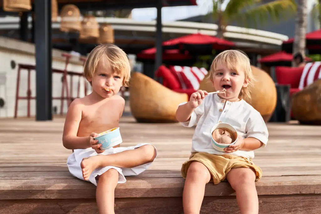 Kinder essen Eis auf einer Holzplattform. Auch Kinder und Familien sind in den LUX Hotels auf Mauritius bestens aufgehoben! Buchen Sie Ihren Familienurlaub bei Fenners Reisen!