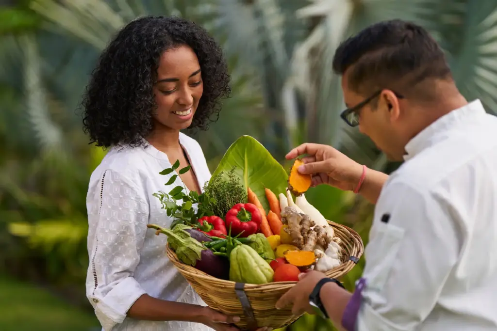 Eine Frau hält einen Korb voll mit frischem Obst und Gemüse - die Kulinarik im LUX Grand Baie ist ausgezeichnet!