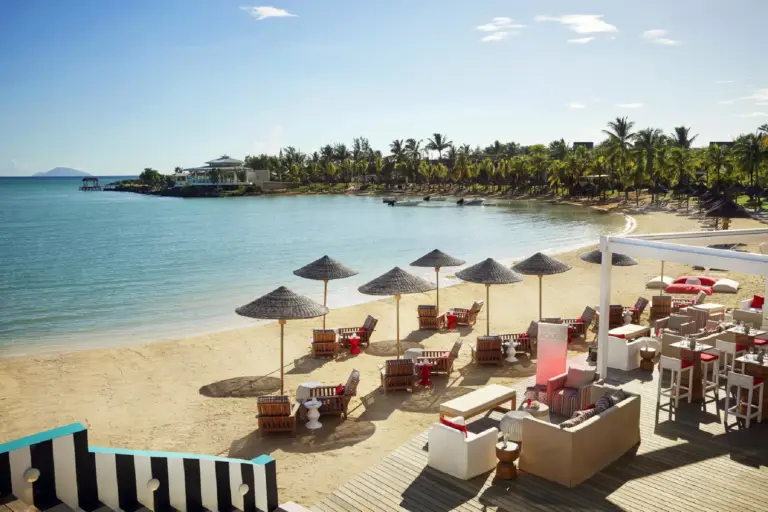 Sonnenschirme und rote Akzente am Strand des LUX Grand Gaube auf Mauritius, buchbar bei Fenners Reisen.