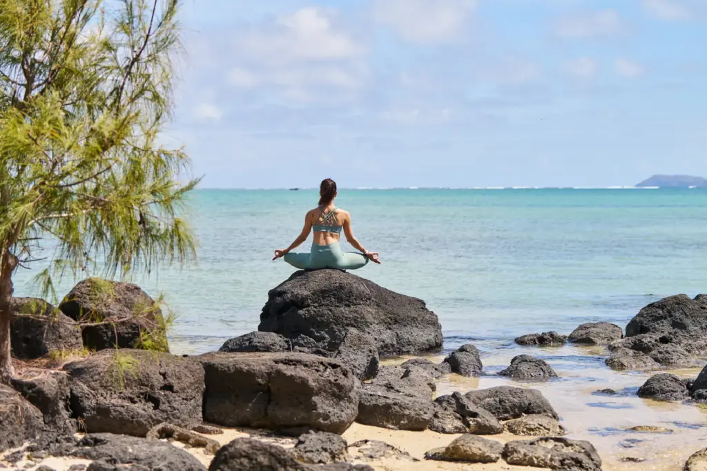 Entspannung pur - eine Frau praktiziert Yoga auf einem ikonischen Felsen vor dem türkisen Meer von Mauritius. Katharina Fenners ist auf Mauritiusreisen spezialisiert und berät Sie individuell und persönlich.
