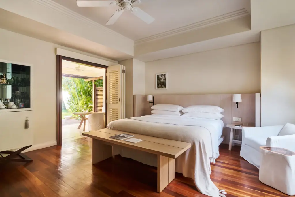 Ein Zimmer im LUX Le Morne Mauritius. Weiß bezogenes Bett, viel Holz und Blick ins Grüne, buchbar bei Fenners Reisen