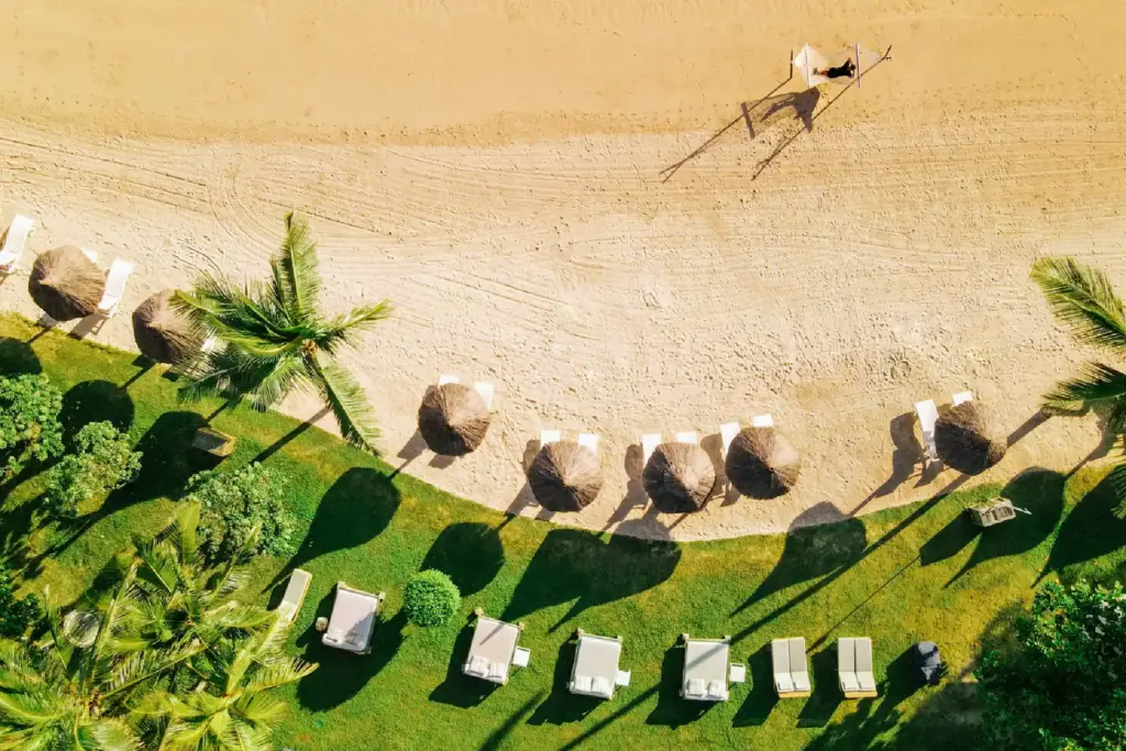 Blick auf die Kontraste von Mauritius - weißer Strand, palmgedeckte Sonnenschirme und tropisches Grün - buchen Sie Ihre Luxusreise Mauritius bei Katharina Fenners!