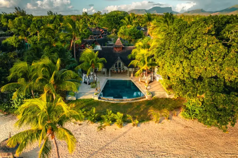 Blick auf eine Villa mit großem Pool, am weißen Sandstrand gelegen und umgeben von üppigem Grün - so luxuriös und intim kann der Villenurlaub auf Mauritius mit Fenners Reisen sein