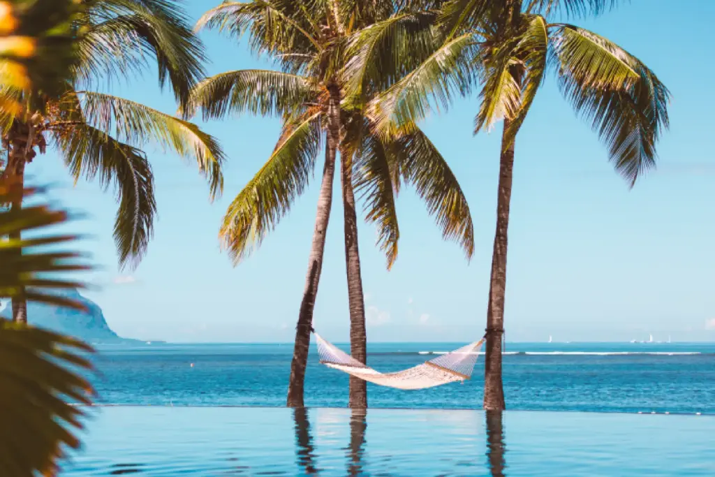 Eine Hängematte zwischen Palmen, das Blau des Pools verschwimmt mit dem Blau des Ozeans, im Hintergrund der Le Morne Berg - ein Urlaub auf Mauritius kann äußerst luxuriös sein. Katharina Fenners berät Sie individuell und persönlich!