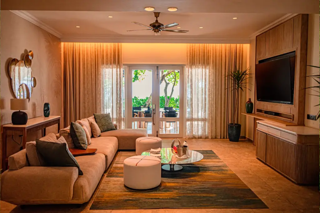 Ein Wohnzimmer mit großem Sofa und Fernseher - stilvoll, mit ruhigen Farben und natürlichen Materialien - so sieht die Presidential Villa im Maradiva Villas Resort und Spa von innen aus. Buchen Sie Ihren Aufenthalt mit Fenners Reisen!