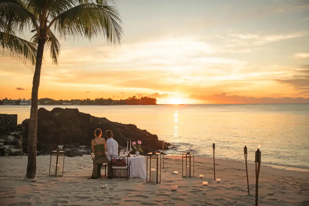 Ein Paar genießt den Sonnenuntergang am einsamen Strand, umringt von romantischen Kerzen - Hochzeiten und Flitterwochen auf Mauritius werden von Katharina Fenners mit größter Sorgfalt geplant. Lassen Sie sich individuell und persönlich beraten!