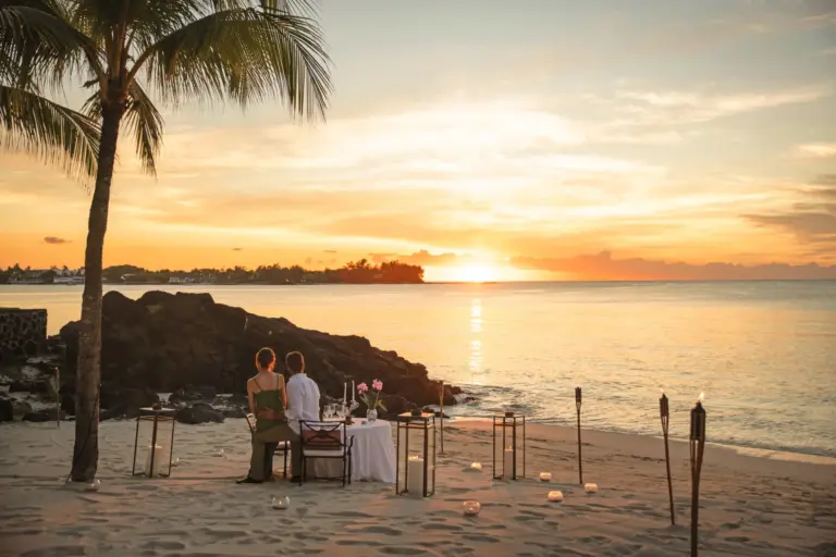 Ein Paar genießt den Sonnenuntergang am einsamen Strand, umringt von romantischen Kerzen - Hochzeiten und Flitterwochen auf Mauritius werden von Katharina Fenners mit größter Sorgfalt geplant. Lassen Sie sich individuell und persönlich beraten!
