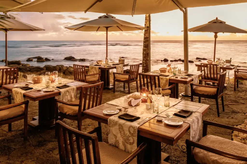 Ein Restaurant im golden schimmernden Abendlicht direkt am Strand. Hier speisen Gäste mit den Füßen im Sand zum Rauschen der Wellen - Katharina Fenners kennt die besten Hotels für Ihren nächsten Urlaub am Indischen Ozean!
