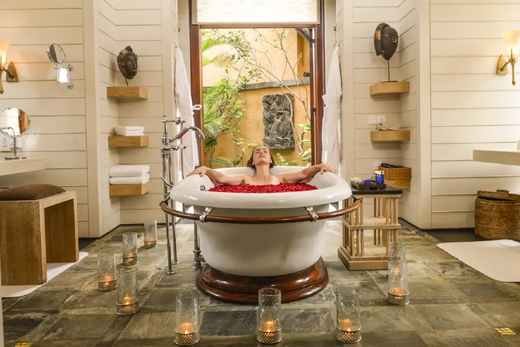 Eine Frau nimmt ein Bad in einer freistehenden Wanne, gefüllt mit einem Meer aus roten Blüten - auf Ihrer Mauritiusreise mit Fenners Reisen muss kaum ein Wunsch offen bleiben!