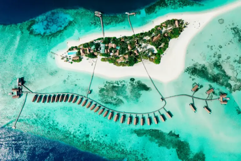 Blick von oben auf Wasservillen, die sich zwischen dem türkisblauen Ozean und strahlend weißen Sandbänken wie Perlen aneinanderreihen - so traumhaft liegt das intime COMO Cocoa Island Resort, buchbar bei Fenners Reisen