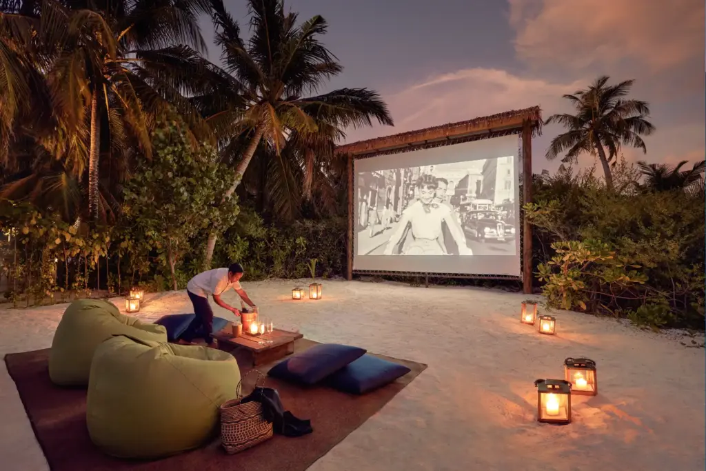 Im weißen, maledivischen Sand ist eine Kinoleinwand unterm Sternenhimmel aufgespannt, grüne Lounge-Sessel laden zwischen flackernden Laternen dazu ein Platz zu nehmen. Unvergessliche Momente wie diesen arrangiert Katharina Fenners für Sie auf den Malediven!