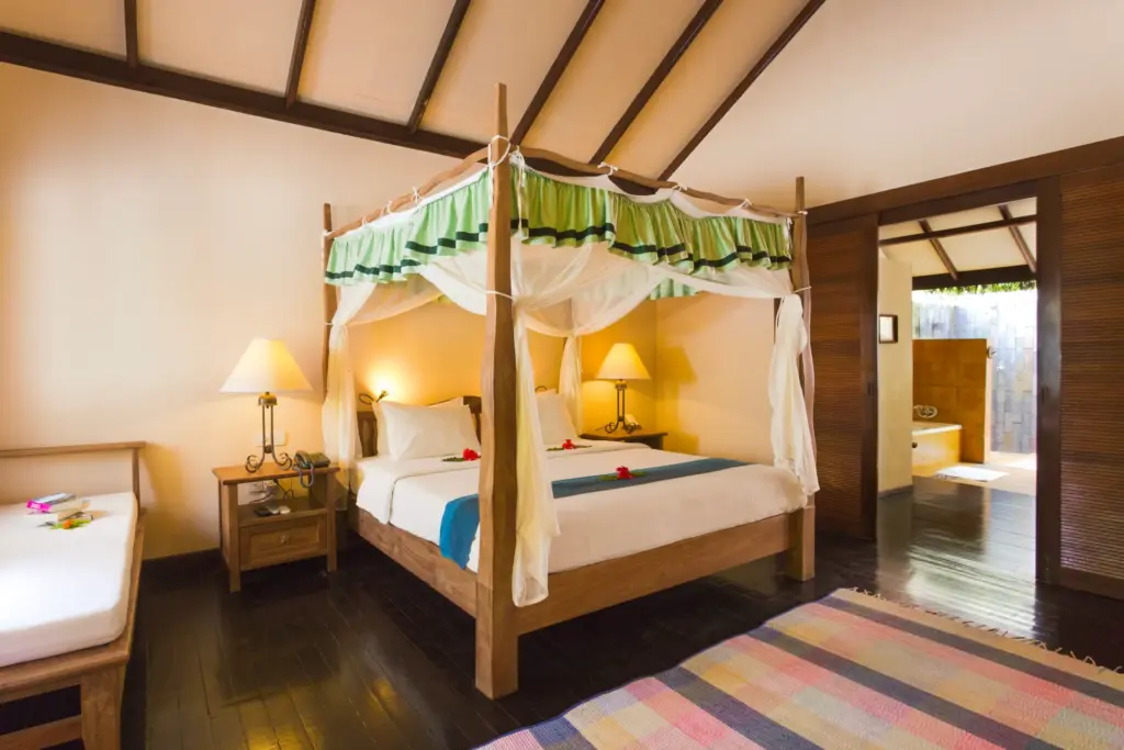 Ein mit Blüten verziertes Doppelbett, im Hintergrund ein offenes Bad mit Wanne und Außendusche - so übernachten Gäste im Filitheyo Island Resort. Katharina Fenners berät Sie individuell!