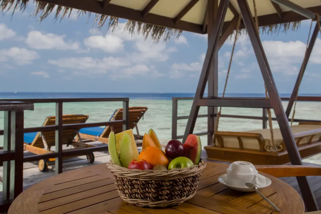 Ein reich gedeckter Obstkorb und zwei gemütliche Liegen warten auf der Terrasse einer Water Villa des Filitheyo Island Resorts, buchbar bei Fenners Reisen