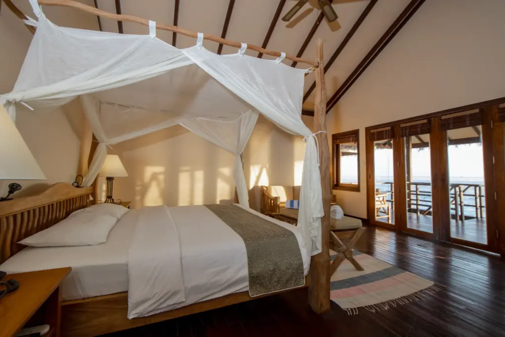 Weiße Schleier umhüllen ein Doppelbett, aus den Fenstern geht der Blick direkt hinaus auf den Indischen Ozean - Wasservillen wie diese sind typisch für die Malediven. Katharina Fenners kennt die besten Unterkünfte über dem Wasser und organisiert Ihren maßgeschneiderten Aufenthalt!