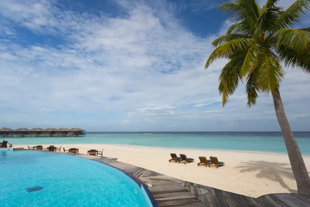 Ein geschwungener hellblauer Pool neben einem einsamen Sandstrand, der seicht in den Indischen Ozean übergeht - Sie sind auf der Suche nach dem perfekten Hotel für einen Malediven-Urlaub? Katharina Fenners ist auf maßgeschneiderte Reisen zu den Trauminseln im Indischen Ozean spezialisiert und berät Sie individuell!