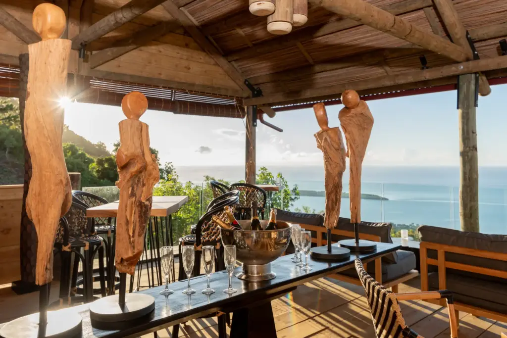 Geschnitzte Skulpturen in einer stilvoll möblierten Bar weit über dem Meerespiegel mit atemberaubendem Rundumblick über den Indischen Ozean - hier speisen Gäste des intimen Hotels Lakaz Chamarel Exclusive Lodge auf Mauritius, buchbar bei Fenners Reisen.