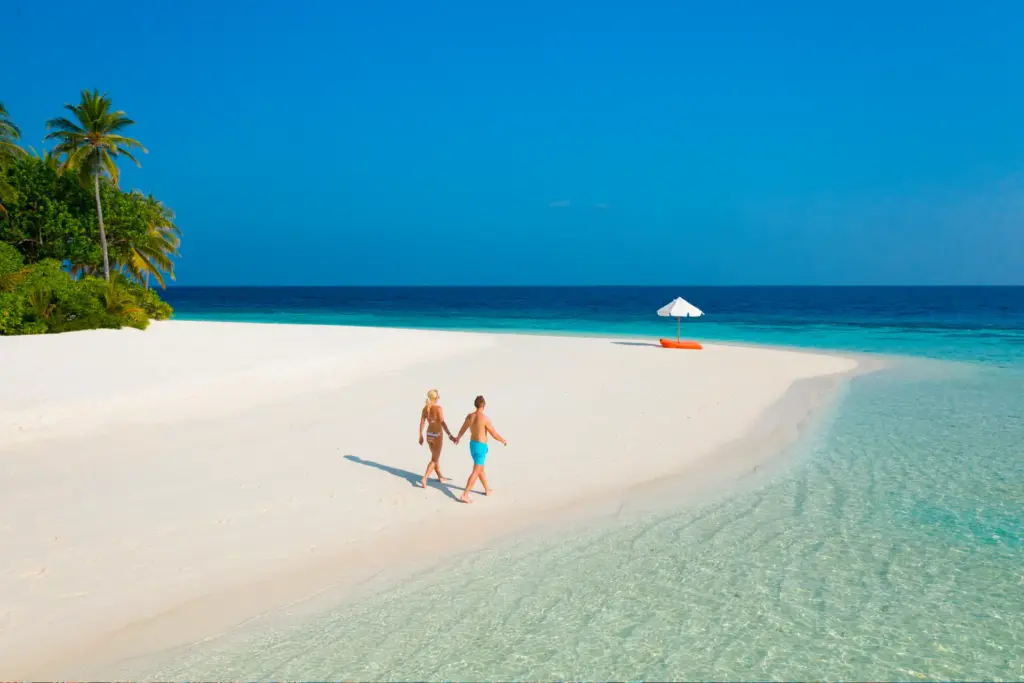 Ein Paar spaziert einen einsamen Sandstrand entlang - das Mirihi Island Resort liegt völlig abgeschieden auf einer winzigen Insel der Malediven und kann bei Fenners Reisen gebucht werden