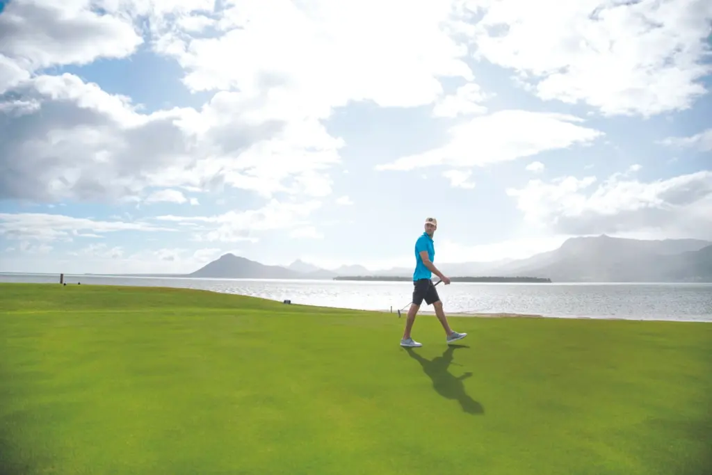 Ein Golfer in idyllischer Kulisse direkt am Meer, im Hintergrund der Berge Le Morne Brabant. Die Trauminsel Mauritius wartet mit hervorragenden Golfplätzen auf! Katharina Fenners organisiert Ihre Golfreise nach Mauritius für Sie.