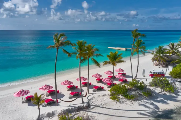 Blick auf den puderweißen Traumstrand mit roten Sonnenschirmen des Seaside Finolhu Baa Atoll Maldives, buchbar bei Fenners Reisen
