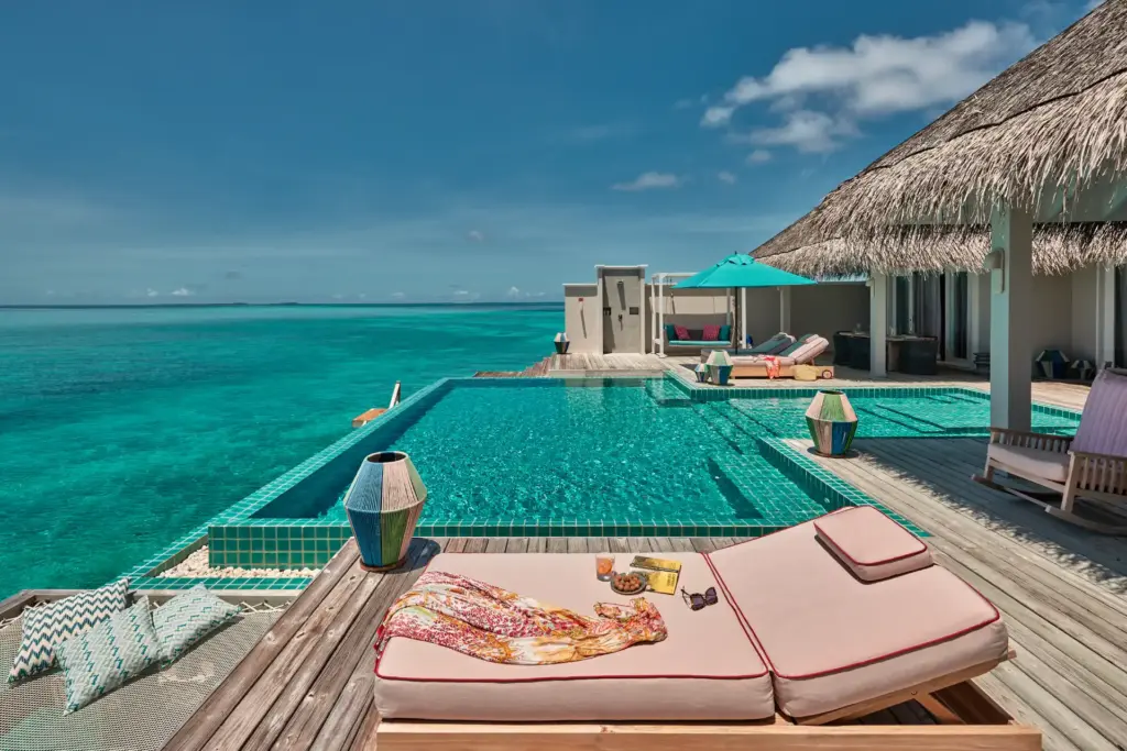 Blau schimmert der Pool einer Wasservilla, eine gemütliche Liege lädt zum Verweilen ein, dahinter schimmert der türkise Ozean - das ist die Rockstar Villa des Seaside Finolhu Baa Atoll Maldives, buchbar bei Fenners Reisen!