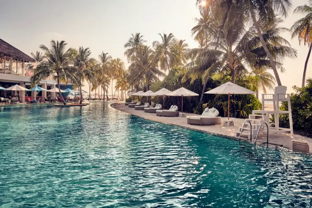 Sonnenschirme und Palmen reihen sich neben einer großzügigen Poollandschaft, während das Abendlicht den Himmel orange färbt - Katharina Fenners ist auf die Trauminseln am Indischen Ozean spezialisiert und kennt die besten Hotels. Lassen Sie sich gleich individuell beraten!