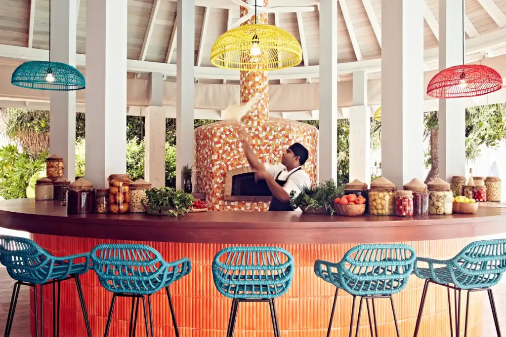 Blaue Barhocker in trendigem Design reihen sich vor der Theke der Pizzeria eines Luxushotels auf den Malediven, wo der Pizzateig vom Pizzabäcker mit Raffinesse in die Luft geworfen wird - viele Hotels auf den Malediven verwöhnen mit exquisiter Kulinarik. Katharina Fenners berät Sie individuell!