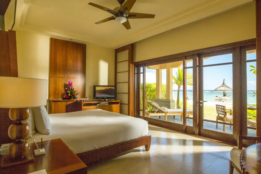 Ein natürlich eingerichtetes Schlafzimmer mit großer Glasschiebetür hinaus auf die Terrasse mit Strandzugang. Buchen Sie einen individuellen Urlaub auf der Trauminsel Mauritius bei Fenners Reisen!