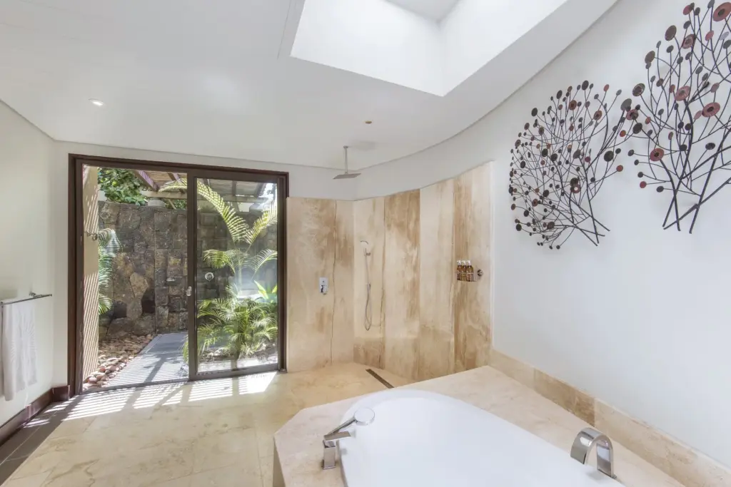 Ein ganz in Marmor gehaltenes Badezimmer mit großer Wanne und bodentiefen Fenstern mit Blick in einen tropisch begrünten Innenhof - Katharina Fenners kennt die besten Hotels auf der Trauminsel Mauritius und berät Sie ganz individuell!