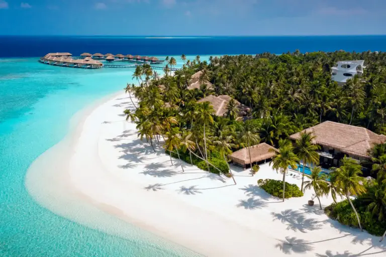 Blick aus der Luft auf die abgeschiedene Privatinsel Velaa Private Island mit ihrem strahlend weißen Strand am türkis schimmernden Ozean - buchbar für Ihren Malediven Luxusurlaub bei Fenners Reisen!