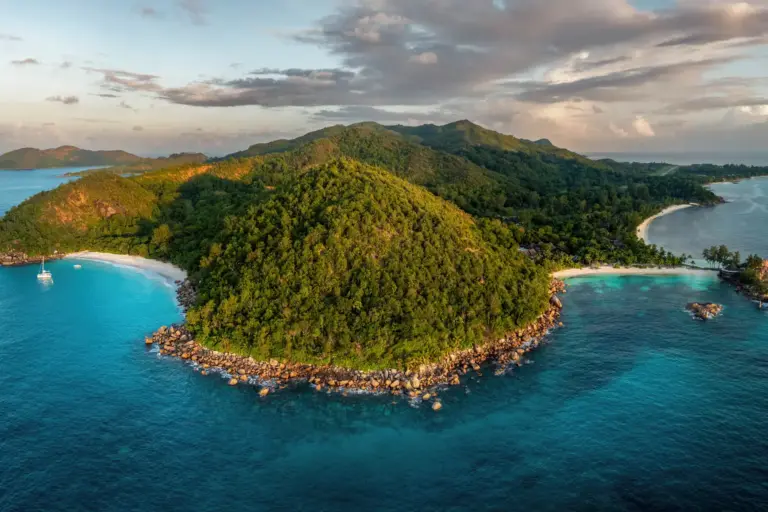 Blick aus der Luft auf die grünen Hänge der Seychellen-Insel Praslin, gesäumt von weißen Stränden. Dieses Naturparadies ist die Kulisse des überaus eleganten Constance Lemuria Seychelles, buchbar bei Fenners Reisen.