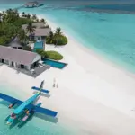 Blick aus der Luft auf ein ikonisches Wasserflugzeug, das halb im türkisen Ozean, halb auf dem puderweißen Sand einer maledivischen Privatinsel gelandet ist. Die Trauminsel Voavah auf den Malediven ist buchbar für exklusive Hochzeitsgesellschaften, intime Familienurlaube und ultraluxuriöse Auszeiten zu zweit. Katharina Fenners berät Sie individuell und organisiert Ihren Urlaub mit maximaler Privatsphäre!