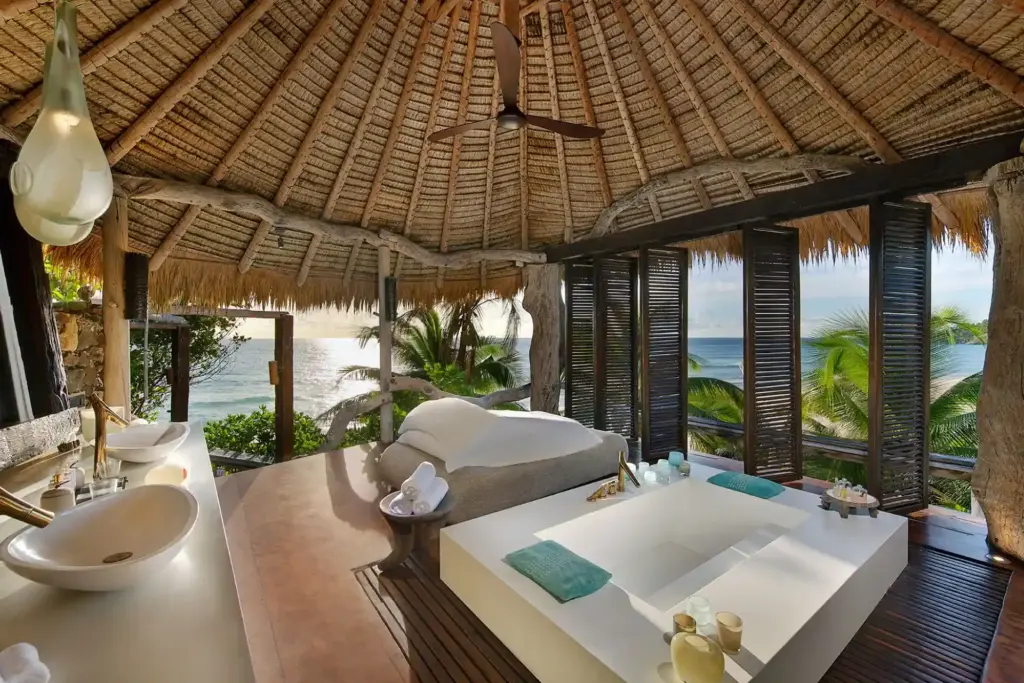 Zentrum dieses weitläufigen Badezimmers mit Blick auf den Indischen Ozean ist eine riesige, in den Boden eingelassene Wanne - so gelingt traumhafte Entspannung im ultraluxuriösen Barfuß-Urlaub, buchbar bei Fenners Reisen