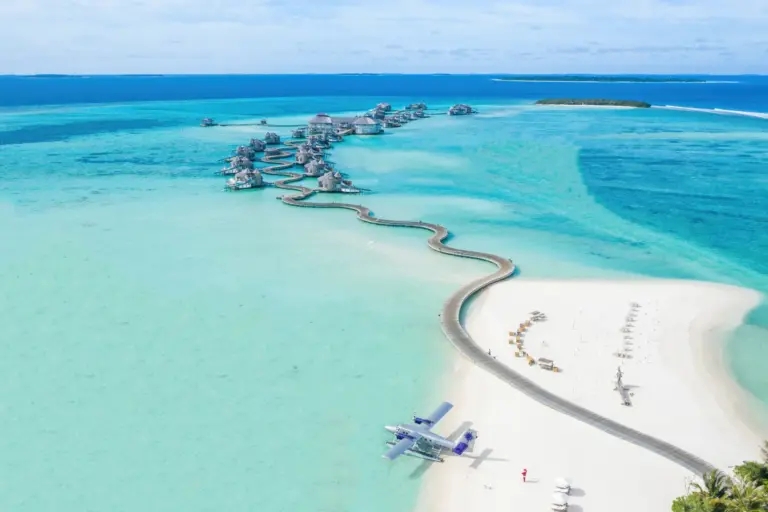 Vogelperspektive auf die paradiesische Kulisse des Soneva Jani Resorts auf den Malediven, buchbar bei Fenners Reisen: Wie eine Perlenschnur ziehen sich die Wasservillen durch das endlose Türkis des Indischen Ozeans, während ein Wasserflugzeug auf dem strahlend weißen Sand der Insel anlegt