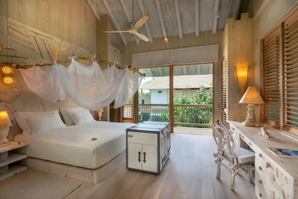 Dieses ganz in hellem Holz möblierte Schlafzimmer eines Island Retreats bietet neben einem großen Bett auch einen Schreibtisch - buchbar für Workations ebenso wie für Familienurlaube auf den Malediven bei Fenners Reisen