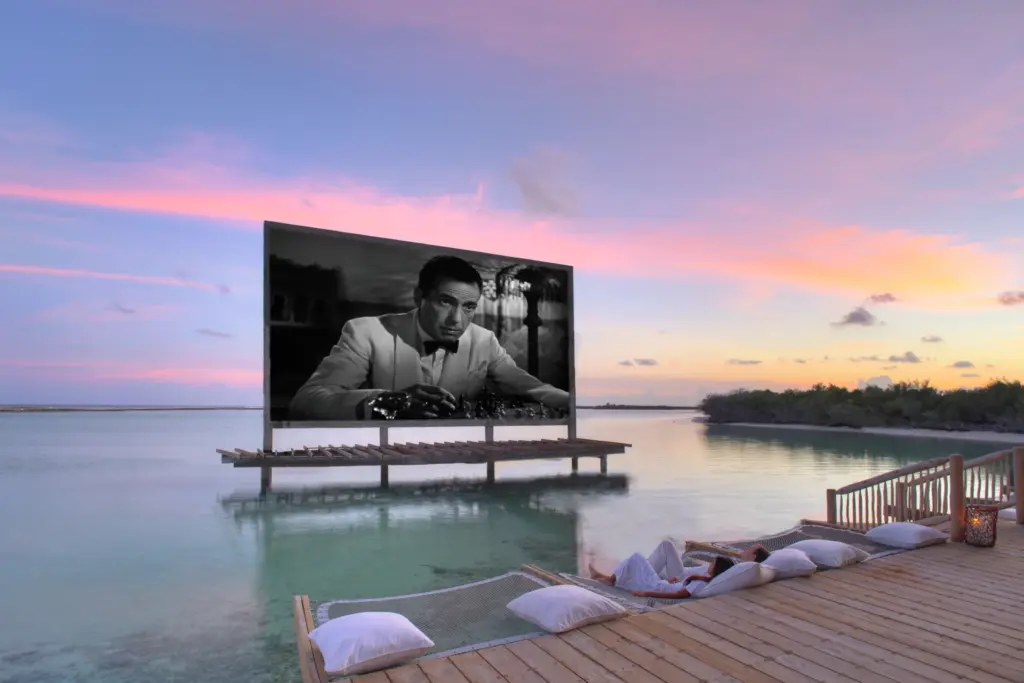 Die legendäre Kinoleinwand des Soneva Jani Resorts auf den Maldiven schwebt über dem Indischen Ozean, zart angehaucht von den Farben des Sonnenuntergangs. Buchen Sie einen besonderen Maledivenurlaub bei der Malediven-Expertin Katharina Fenners, gemütliche Loungekissen und Wasser-Hängematten warten bereits auf Sie - für große Kino-Momente im Luxusurlaub nach Maß.