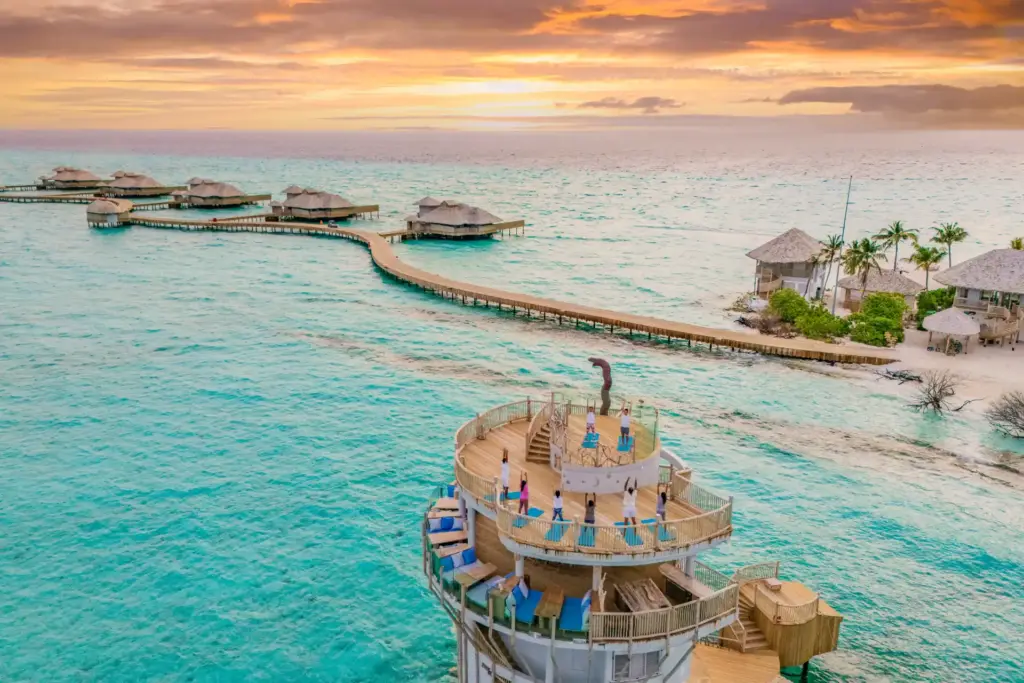 Auf der Aussichtsplattform des Soneva Secret praktiziert eine Gruppe Yoga, während die untergehende Sonne den Indischen Ozean in spektakuläres Orange taucht - der Aufenthalt ist buchbar bei Fenners Reisen