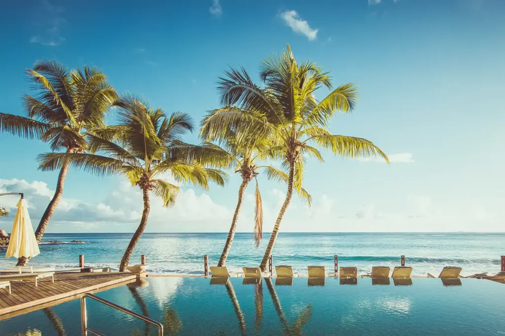 Palmen spiegeln sich im glitzernden Infinity Pool des CaranaBeach Hotels auf den Seychellen, nur eine Reihe von Liegestühlen trennen ihn vom gleich dahinter beginnenden Indischen Ozean. Buchen Sie einen maßgeschneiderten Aufenthalt für Ihren Seychellen Urlaub oder Ihre Seychellen Hochzeitsreise bei Fenners Reisen!