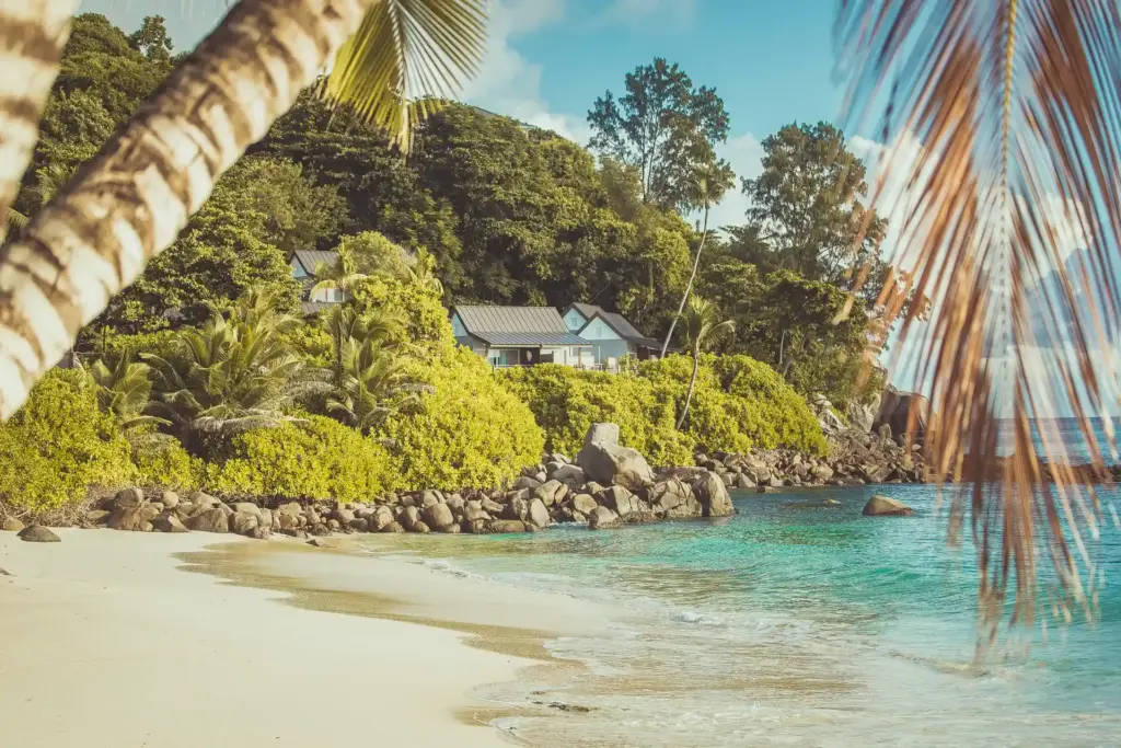 Blick aus der Ferne auf ein Ocean View Chalet des CaranaBach Hotels auf den Seychellen - in idyllischer Hanglange direkt über den ikonischen Felsen, die den traumhaft weißen Strand begrenzen. Buchbar für Ihre Seychellen Auszeit oder Seychellen Hochzeitsreise bei Fenners Reisen.
