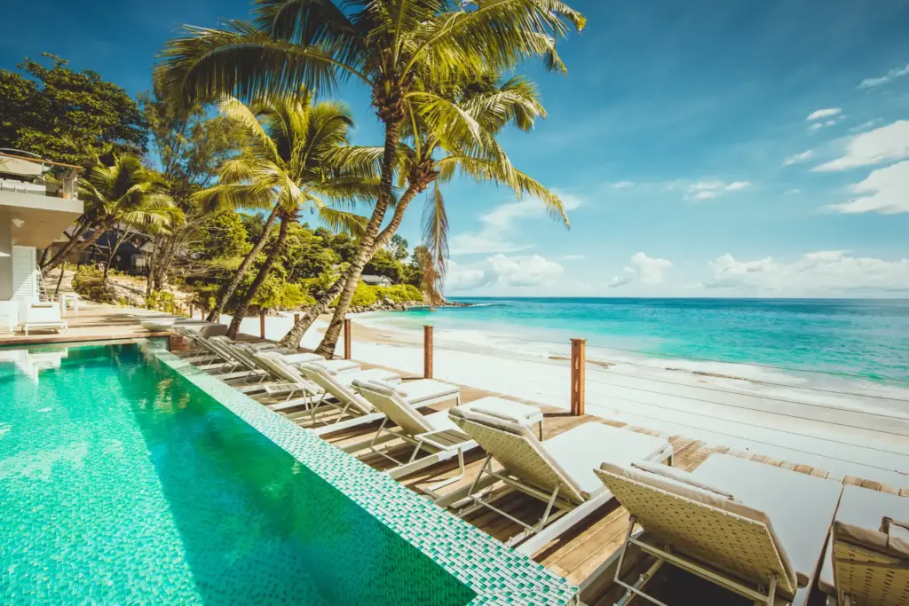Blick auf den Pool und Strand vor dem intimen CaranaBeach Hotel im Norden der Seychelleninsel Mahé - ein echtes Paradies für Ruhesuchende, buchbar bei Fenners Reisen