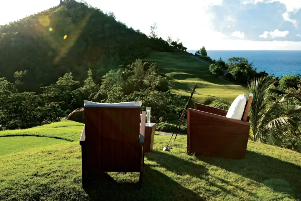 Zwei Sessel und Golfschläger auf einem Hügel vor der imposanten Kulisse der Seychellen-Insel Praslin. Die Seychellen sind ein hervorragendes Ziel für Golfliebhaber, maßgeschneidert und individuell organisiert wird die Seychellen Golfreise von Fenners Reisen.
