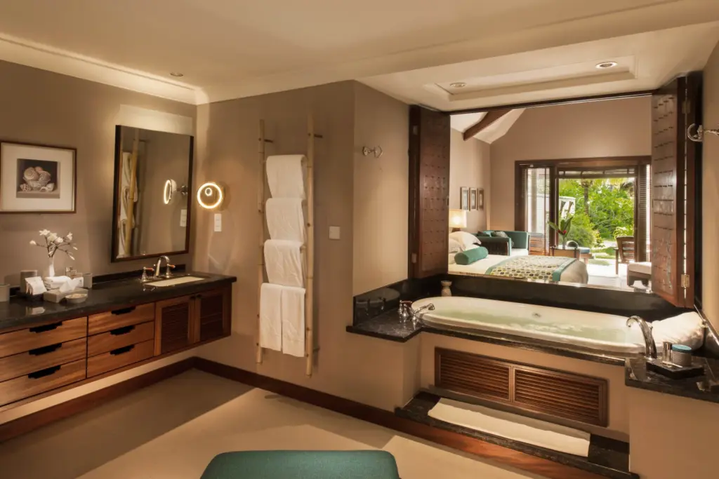 Dank geschickt platzierter Fenster genießen Gäste dieser Seychellen-Villa freien Blick von der Badewanne über das angrenzende Schlafzimmer bis hinaus ins tropische Grün - buchen Sie einen maßgeschneiderten Aufenthalt auf der Seychellen-Insel Praslin bei Fenners Reisen!