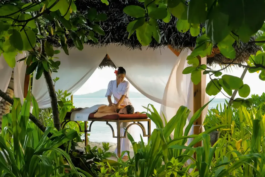 Eine Frau genießt eine wohltuende Massage vor der atemberaubenden Naturkulisse der Seychellen-Insel Praslin. Buchen Sie luxuriöse Entspannung im Constance Lemuria Seychelles bei Fenners Reisen!
