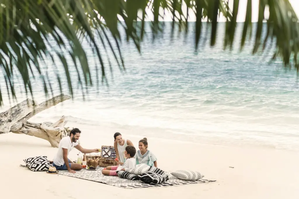 Eine Familie macht Picknick am völlig einsamen, puderweißen Strand der intimen Seychellen-Privatinsel Desroches. Der Aufenthalt ist buchbar für Ihren luxuriösen Seychellen Familienurlaub bei Fenners Reisen!
