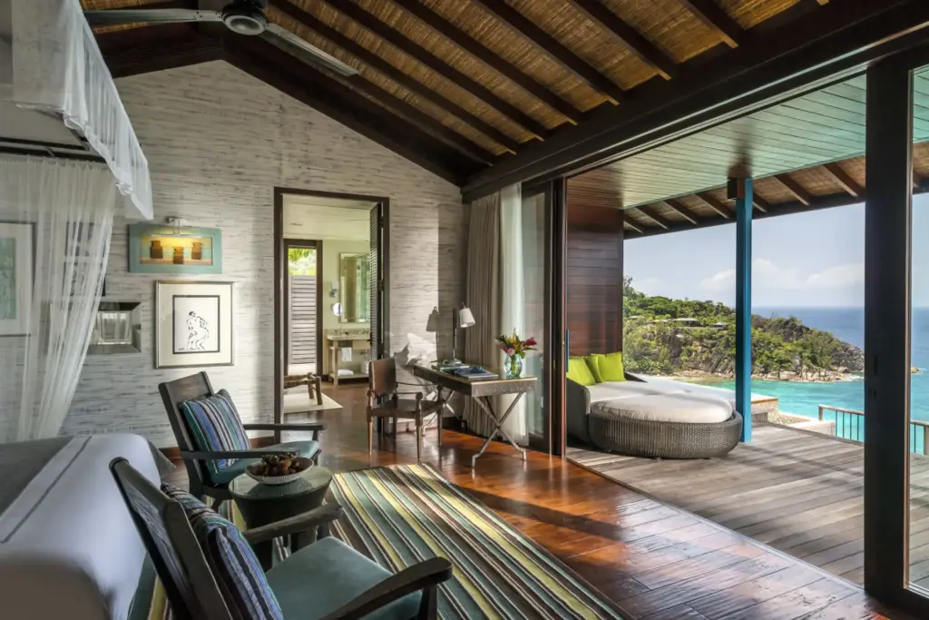 Eine ausgesprochen stilvoll möblierte Villa mit hohen Decken, Sesseln und offenem Blick zur Terrasse und dem dahinterliegenden Indischen Ozean. Sie sind auf der Suche nach einem exklusiven Resort für Ihren Seychellen Luxusurlaub? Katharina Fenners ist Expertin für die Inseln im Indischen Ozean und berät Sie individuell und persönlich!